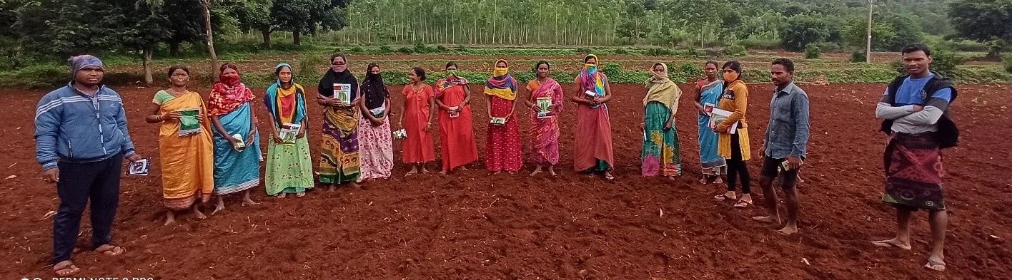 Women farmers holding seed packets in a ploughed field
